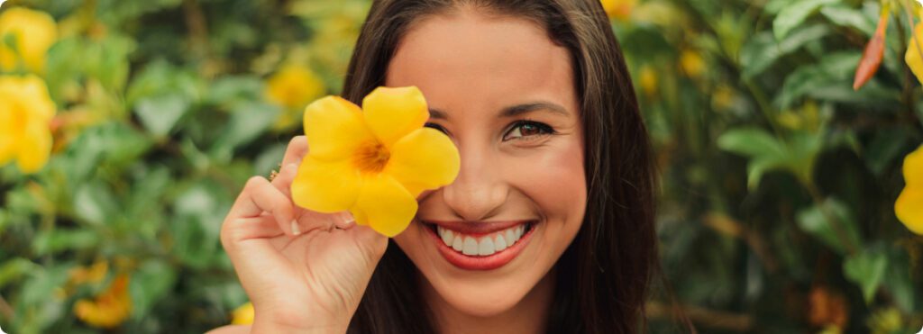 A woman happily holds a yellow flower, radiating joy and warmth with her smile.