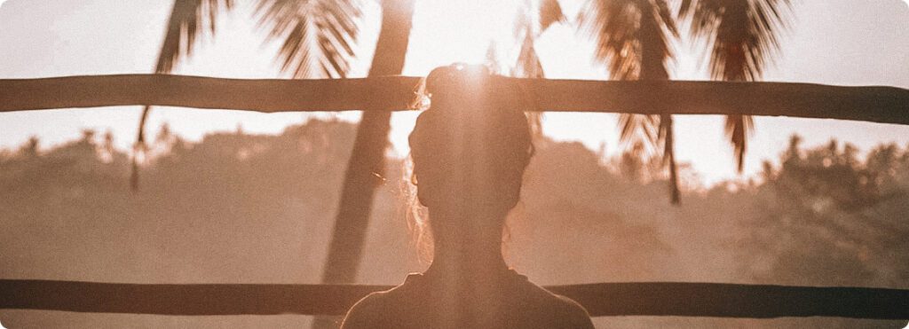 A woman meditating on a wooden deck in the sun.