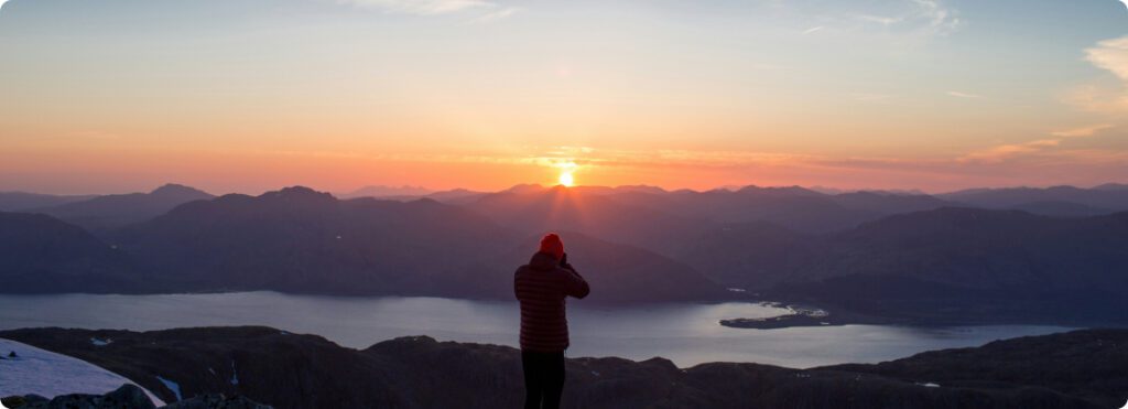 A person standing on a mountain peak, basking in the golden glow of a sunset.