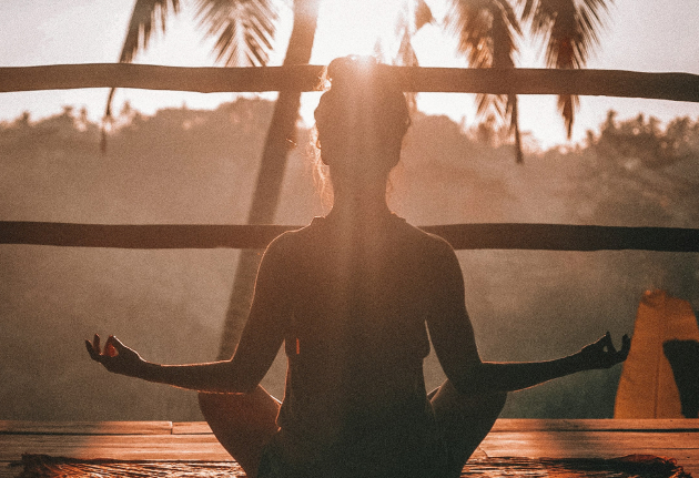 A woman meditating on a wooden deck in the sun.