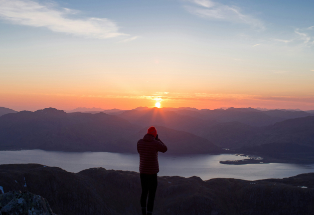 A person standing on a mountain peak, basking in the golden glow of a sunset.